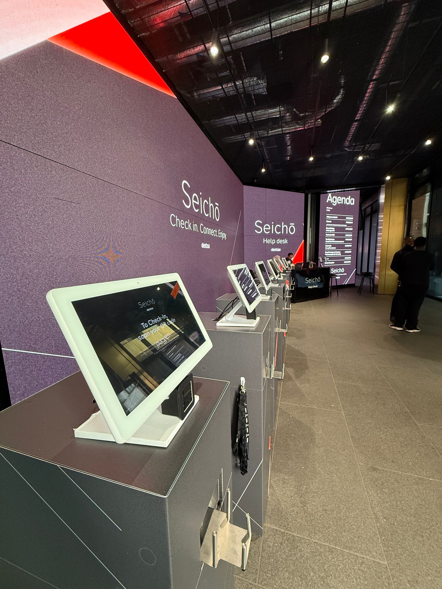 Row of branded Xtag check-in kiosks with lanyards